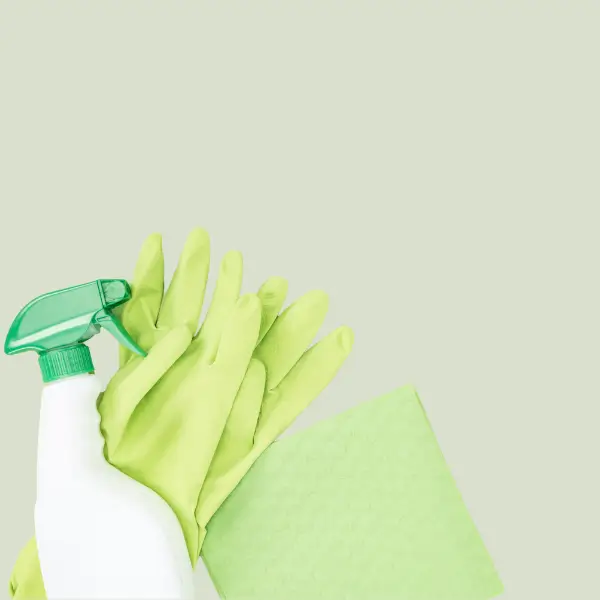 Green cleaning gloves, spray bottle, and cloth on a light green background representing eco-friendly cleaning by Comforts Cleaning Services in San Diego.