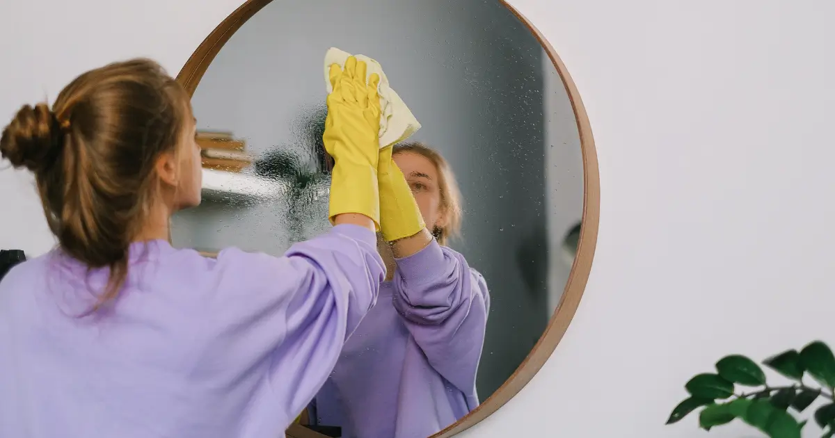 Woman cleaning a mirror at home while following a daily cleaning routine.