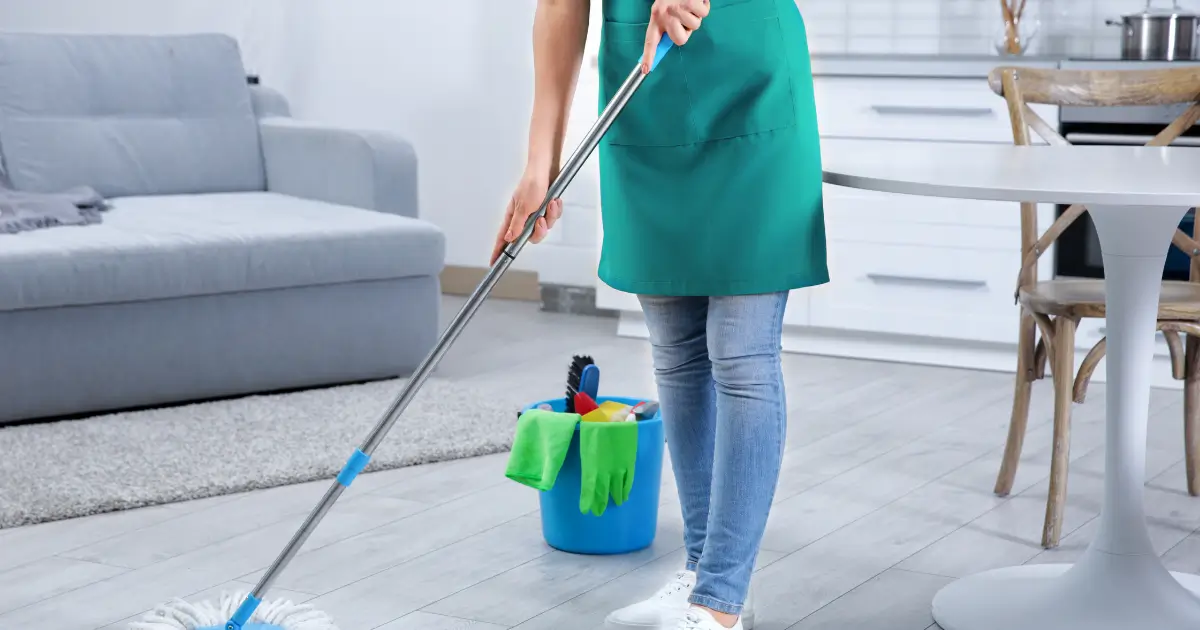 Professional cleaner mopping a renovated living room floor with cleaning supplies in a bucket nearby