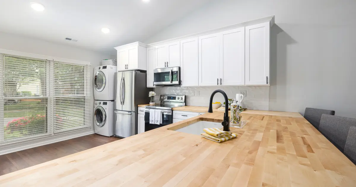 A clean modern kitchen in temporary housing with white cabinets, stainless steel appliances, and a wooden countertop, showing an organized and hygienic living space