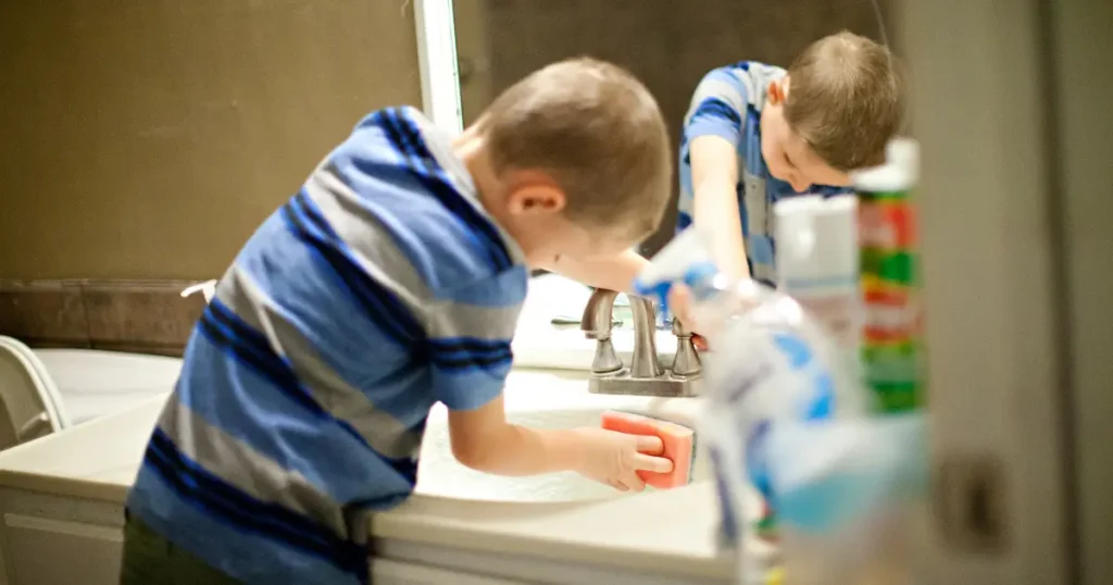 Child cleaning a bathroom sink with help from a parent, promoting healthy cleaning habits for a clean and tidy home with kids