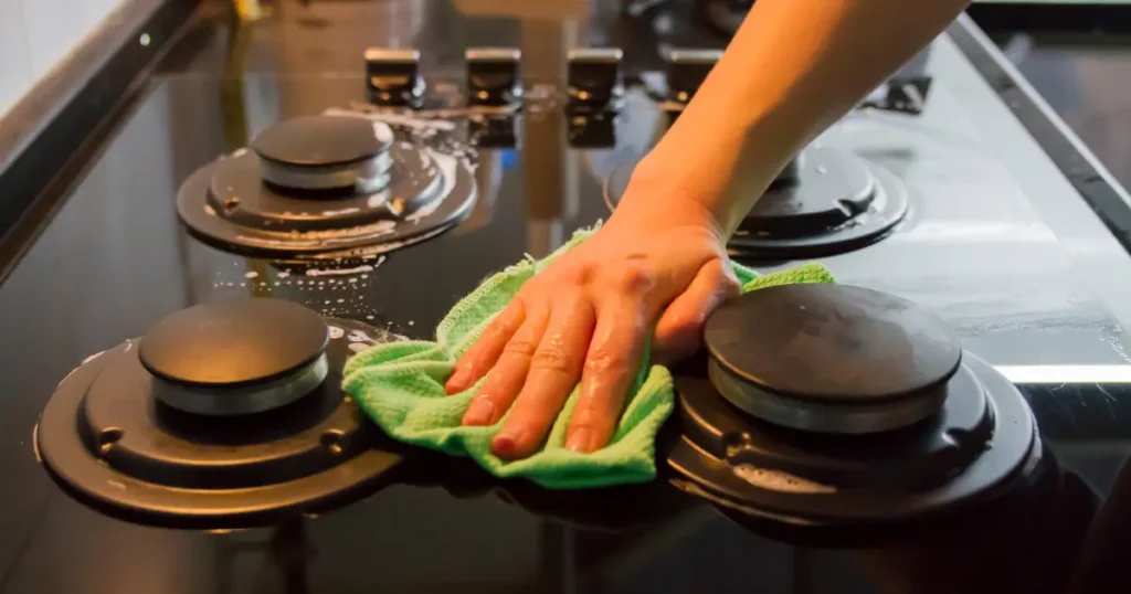 Person wiping a kitchen stovetop during a weekly deep cleaning routine