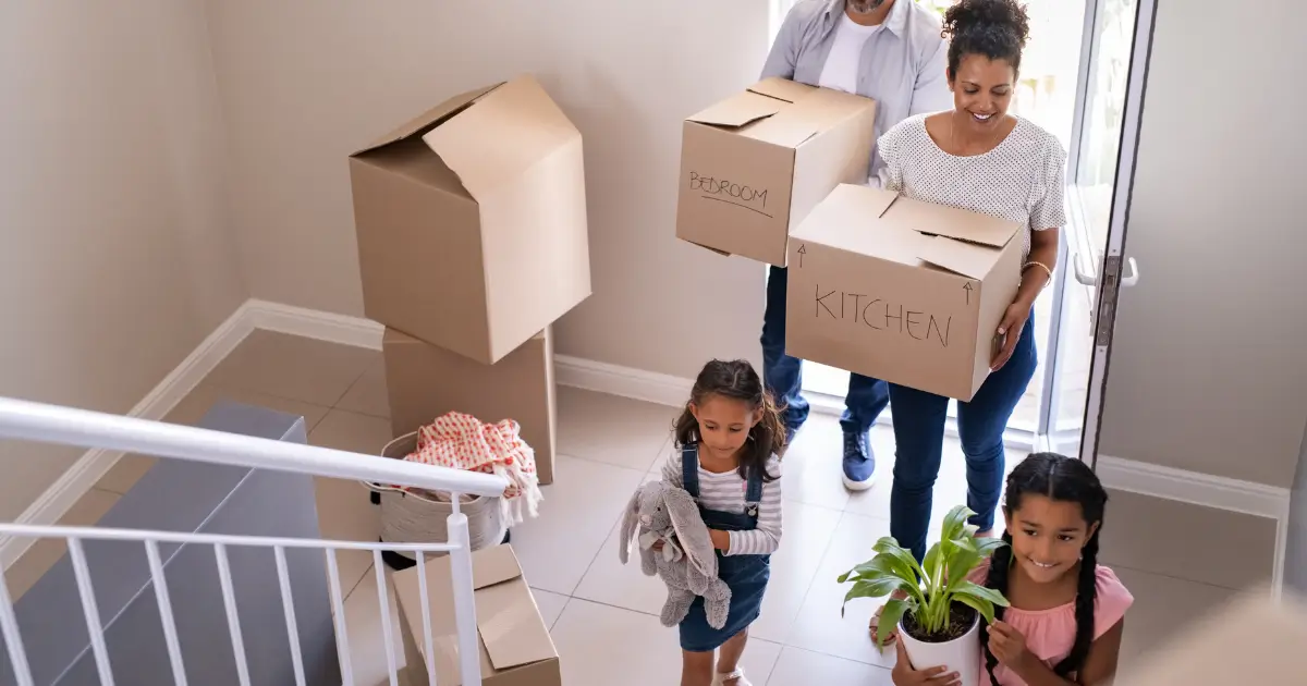 A family carrying moving boxes and plants into a new home during move-in.