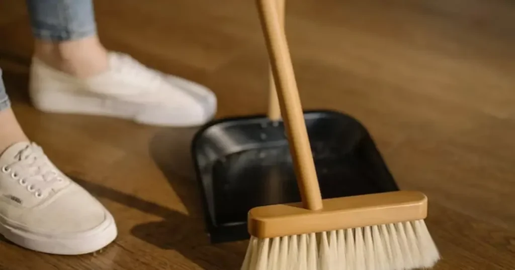 Person sweeping the floor with a broom and dustpan during move-out cleaning to prepare the home for the next occupant.