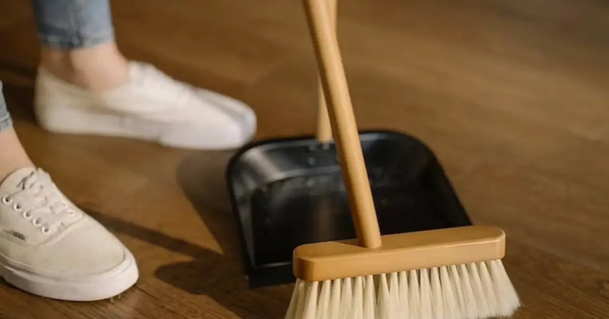 Person sweeping the floor with a broom and dustpan during move-out cleaning to prepare the home for the next occupant.