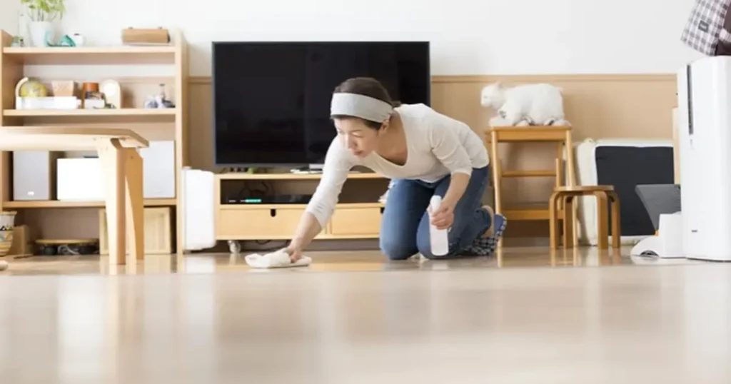 Woman kneeling on the floor preparing her home for a deep cleaning by wiping and organizing the living room.